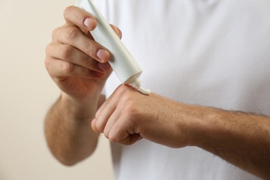 Photo of Man applying cream from tube onto hand on beige background, closeup