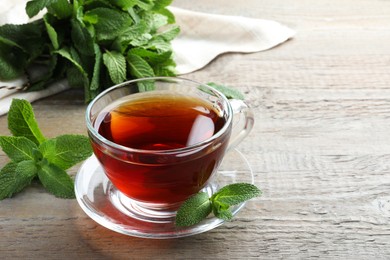 Cup of hot aromatic tea with mint on wooden table. Space for text