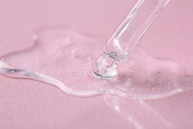 Dripping cosmetic serum from pipette onto pink background, macro view