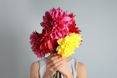 Photo of Woman holding bouquet of beautiful dahlia flowers against gray background