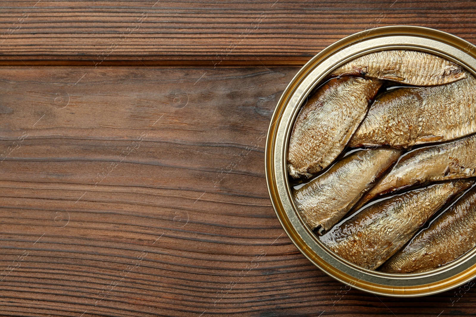 Photo of Open tin can of sprats on wooden table, top view. Space for text