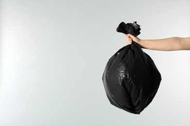 Photo of Woman holding trash bag full of garbage on light grey background, closeup. Space for text