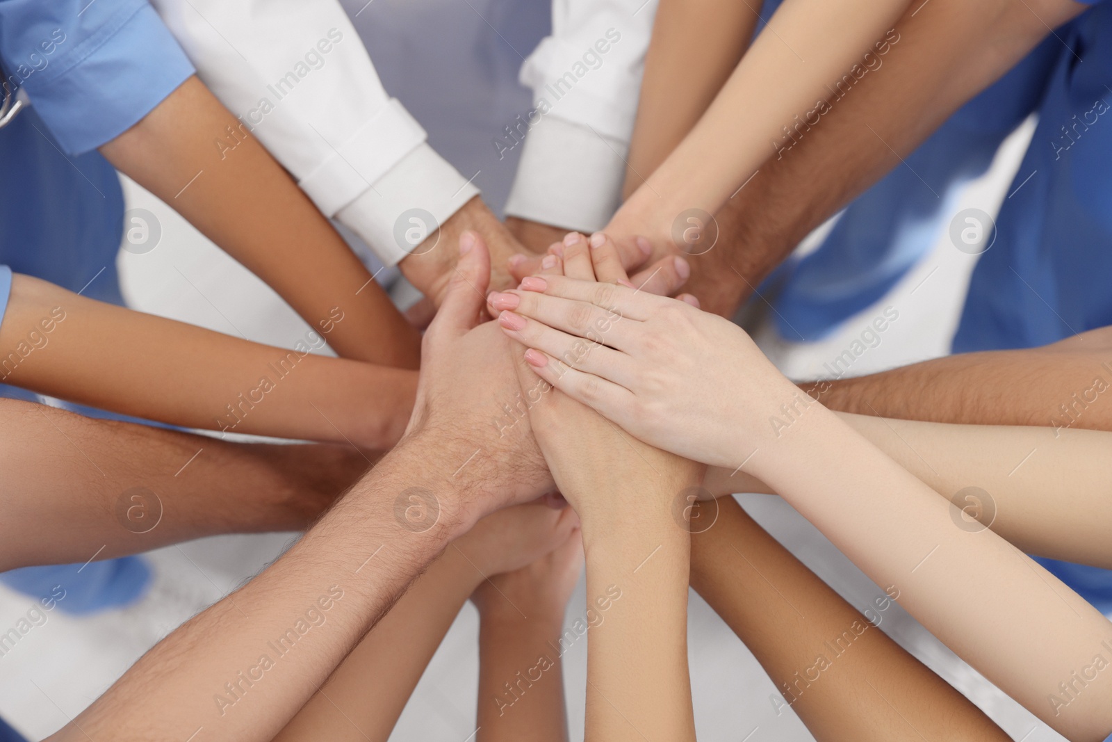 Photo of Doctor and interns stacking hands together indoors, closeup