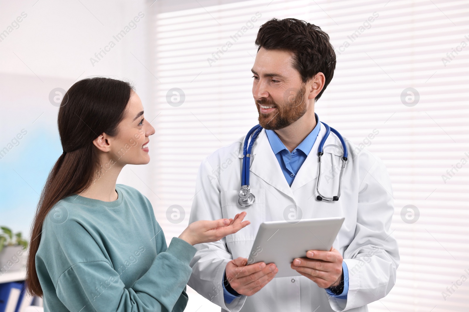 Photo of Doctor with tablet consulting patient during appointment in clinic