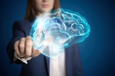 Image of Young woman pointing at digital image of brain on blue background, closeup