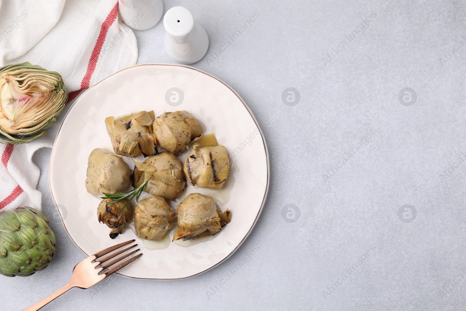 Photo of Delicious pickled artichokes with rosemary served on light grey table, flat lay. Space for text