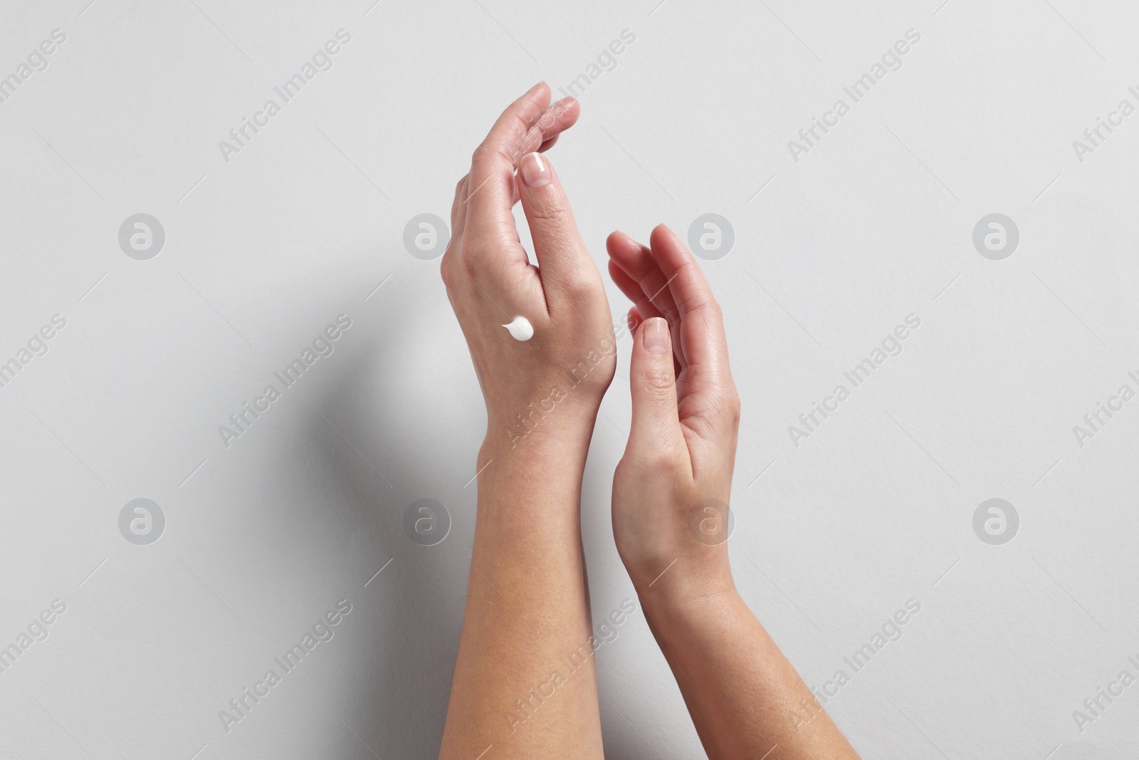 Photo of Woman with cosmetic cream on hand against light grey background, top view