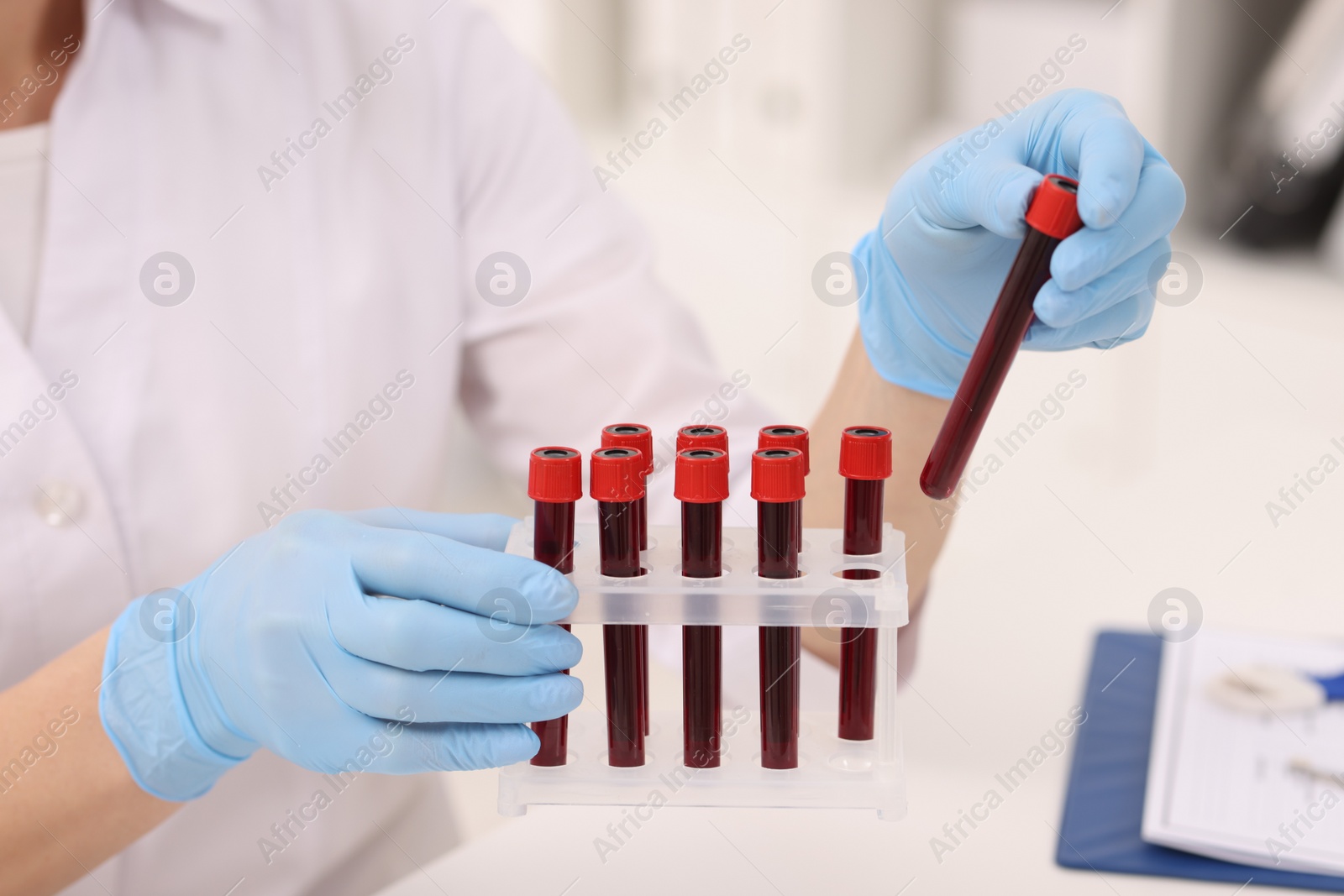 Photo of Doctor with samples of blood in test tubes at white table, closeup