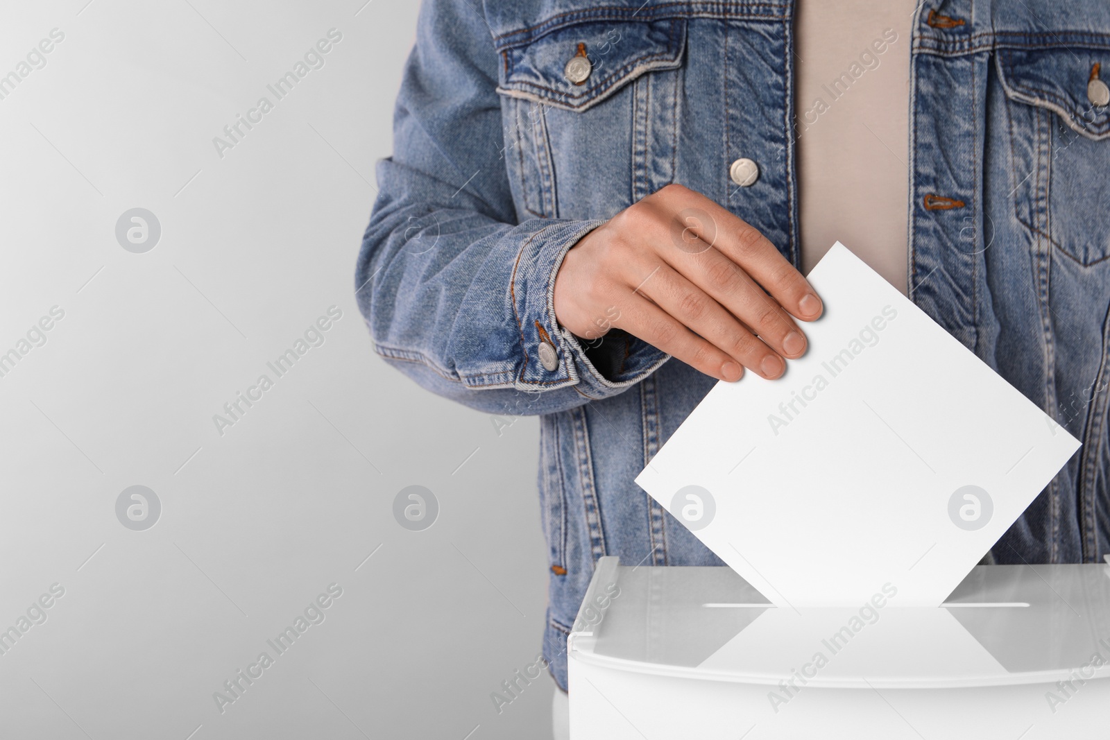 Photo of Man putting his vote into ballot box on light grey background, closeup. Space for text