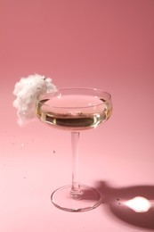 Tasty cocktail in glass decorated with cotton candy on pink background