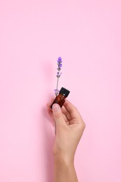 Woman with bottle of lavender essential oil and flower on pink background, closeup