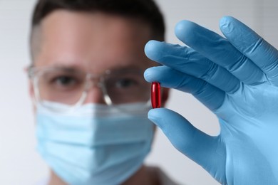 Photo of Doctor holding pill on light background, selective focus. Space for text