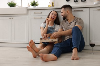Photo of Affectionate young couple eating pizza in kitchen. Space for text