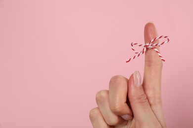 Woman showing index finger with tied bow as reminder on pink background, closeup. Space for text