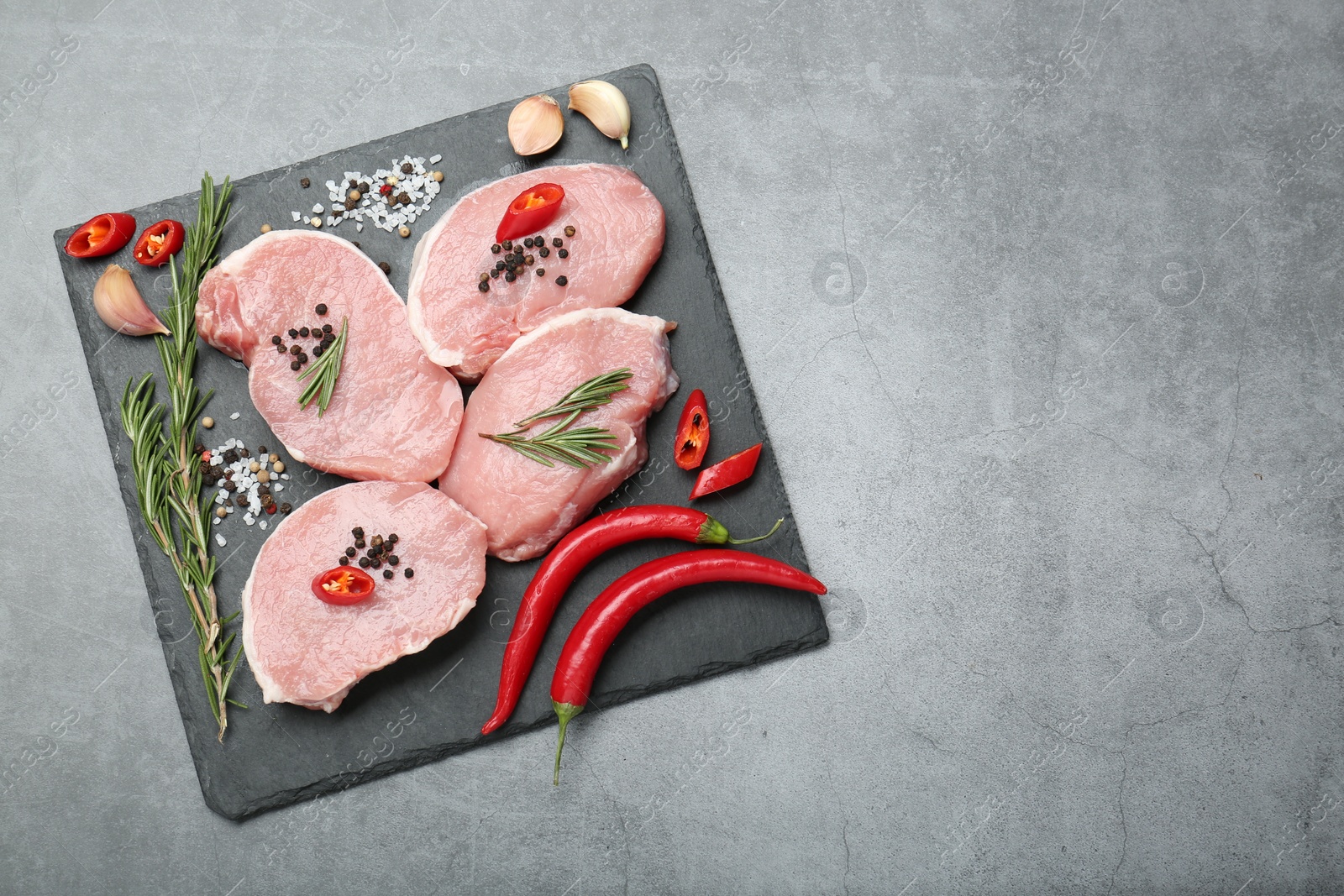 Photo of Pieces of raw pork meat, chili peppers and spices on grey table, top view. Space for text