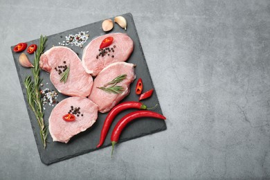 Photo of Pieces of raw pork meat, chili peppers and spices on grey table, top view. Space for text