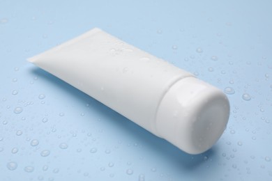 Wet tube of face cleansing product on light blue background, closeup