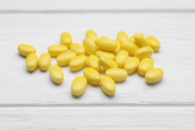 Photo of Many yellow dragee candies on white wooden table, closeup