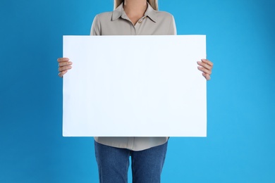 Woman holding blank poster on blue background, closeup