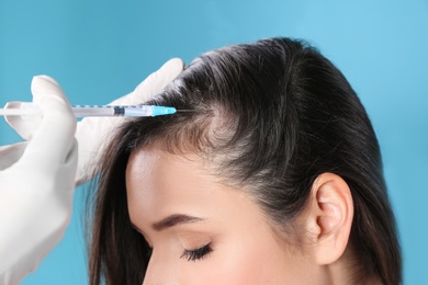 Young woman with hair loss problem receiving injection on color background, closeup