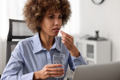 Photo of Woman taking pill while suffering from headache at workplace in office