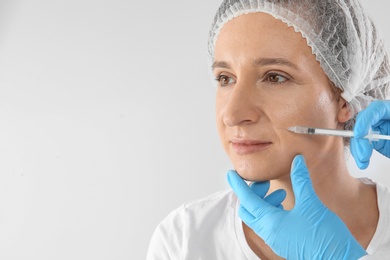 Photo of Mature woman getting facial injection and space for text on white background. Cosmetic surgery concept
