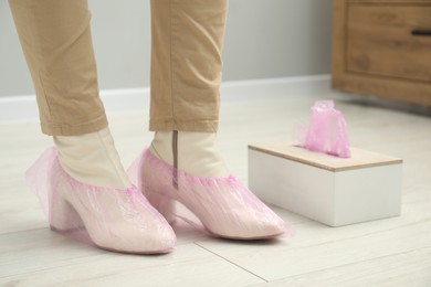 Photo of Woman wearing pink shoe covers onto her boots indoors, closeup