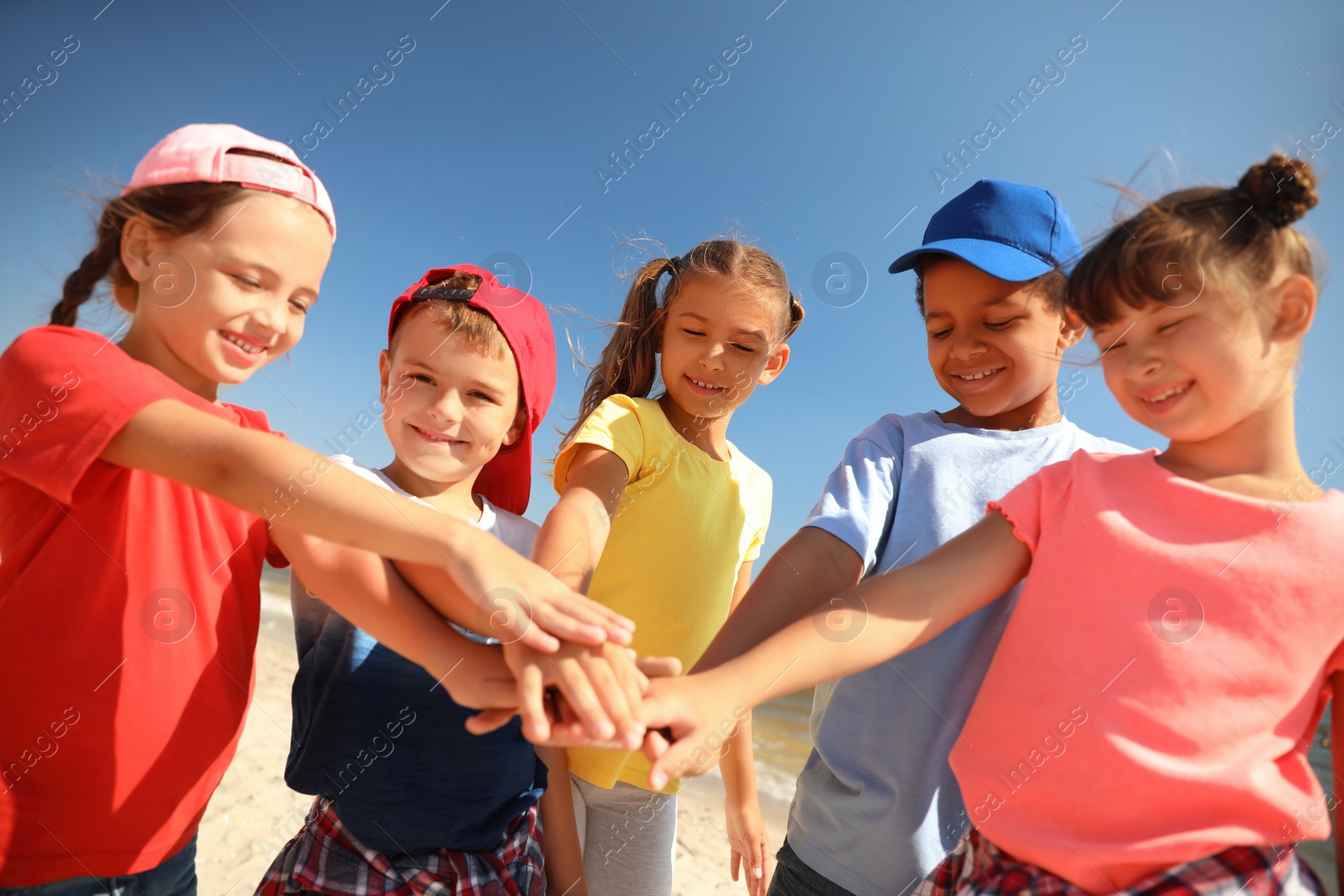 Photo of Group of children putting hands together outdoors on sunny day. Summer camp