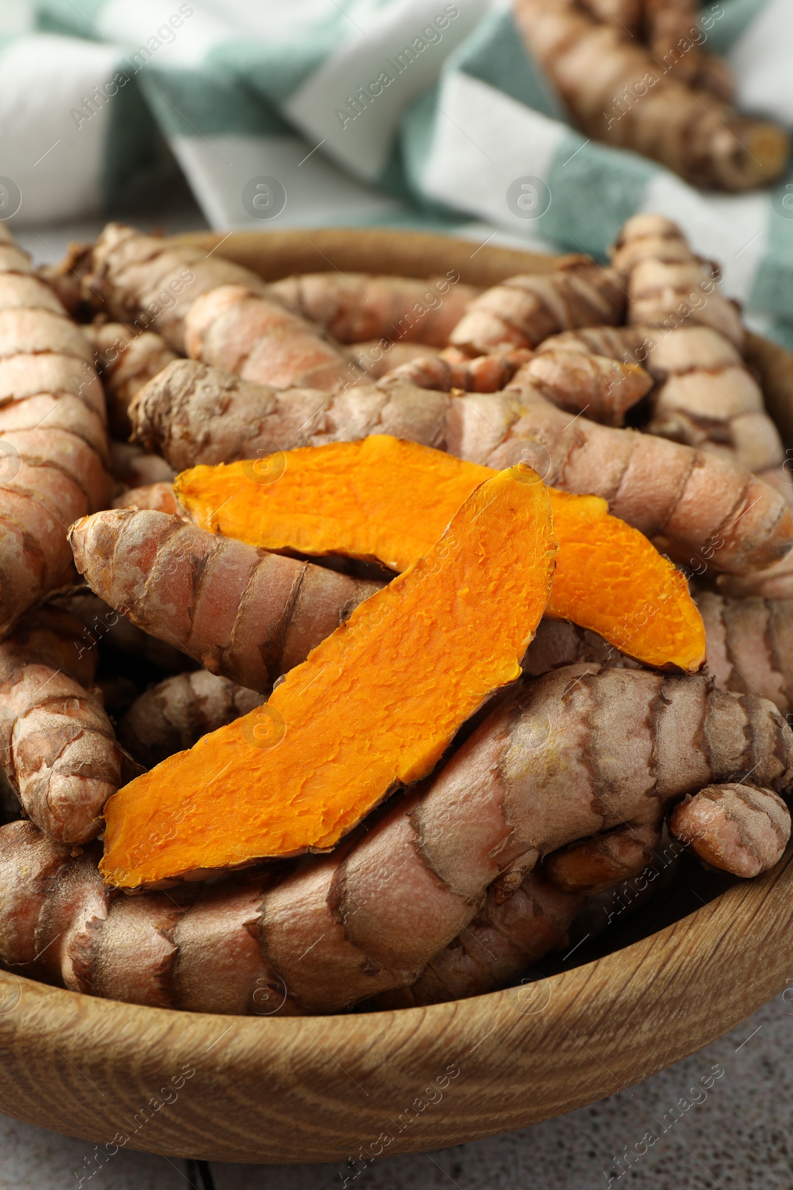 Photo of Bowl with whole and cut turmeric roots on table, closeup