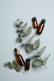 Aromatherapy. Bottles of essential oil and eucalyptus leaves on light grey background, flat lay