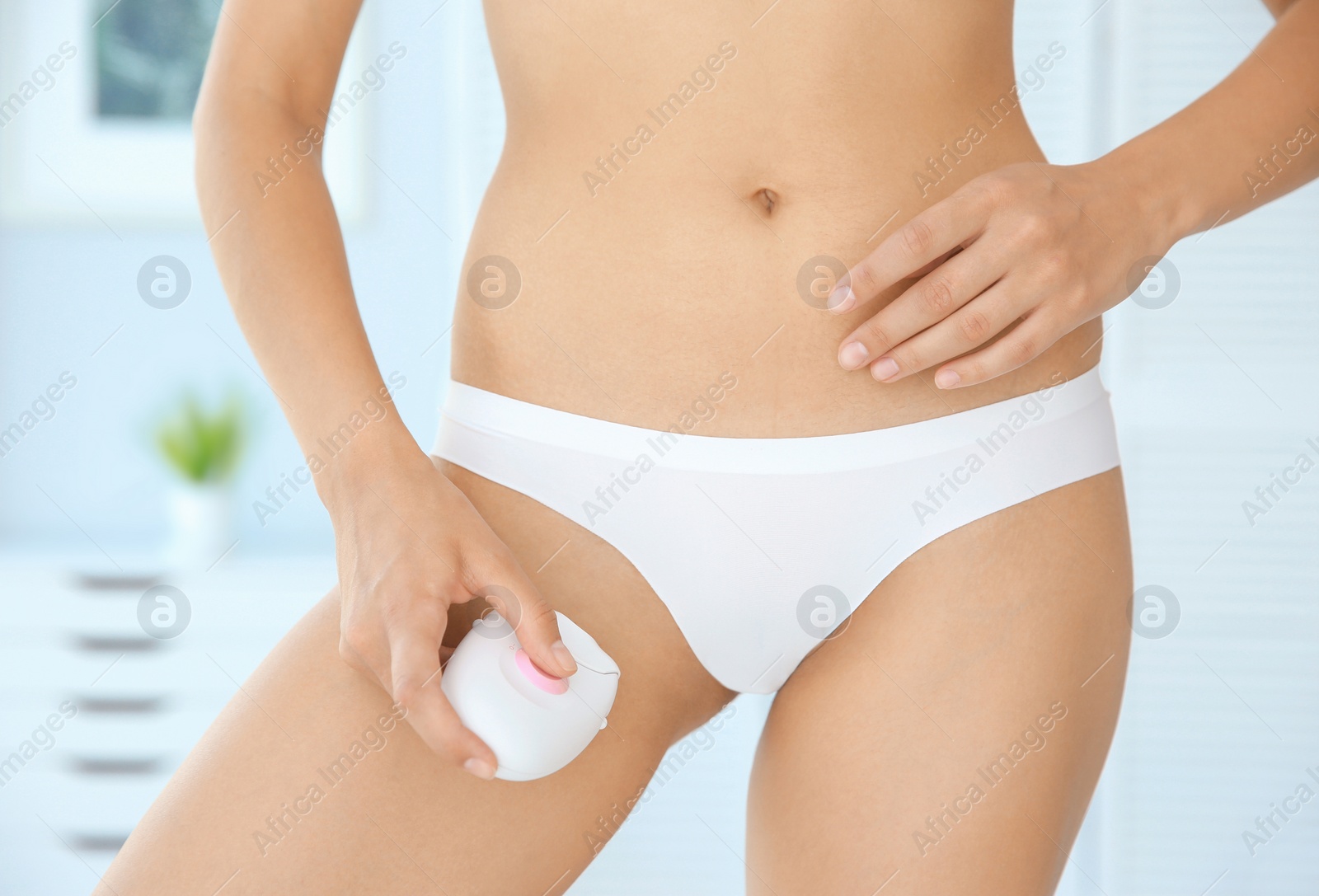 Photo of Sexy young woman epilating bikini area indoors
