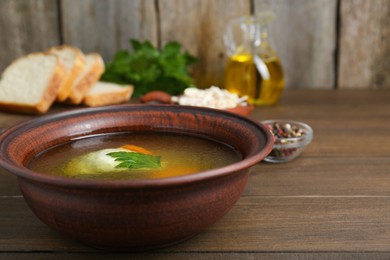 Delicious chicken bouillon with carrot and parsley in bowl on wooden table, closeup