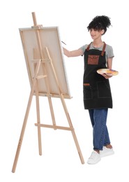 Young woman painting on easel with canvas against white background