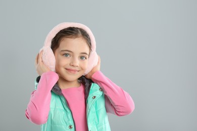 Photo of Cute girl wearing stylish earmuffs on grey background. Space for text