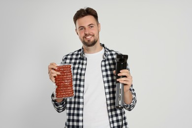 Photo of Smiling man holding sous vide cooker and sausages in vacuum pack on beige background