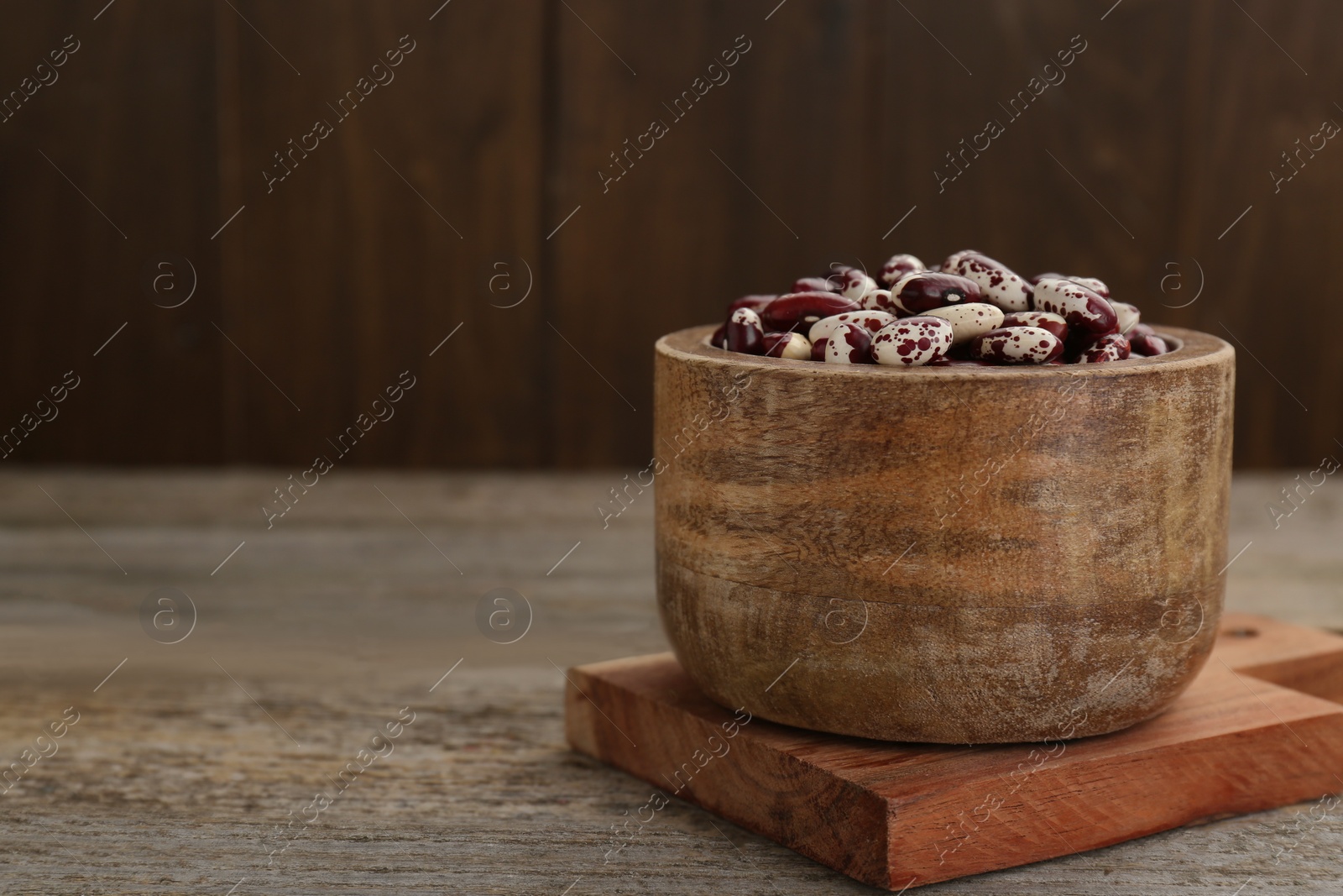 Photo of Bowl with dry kidney beans on old wooden table. Space for text