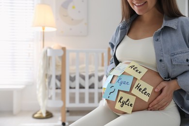 Photo of Pregnant woman with different baby names on belly at home, closeup. Space for text