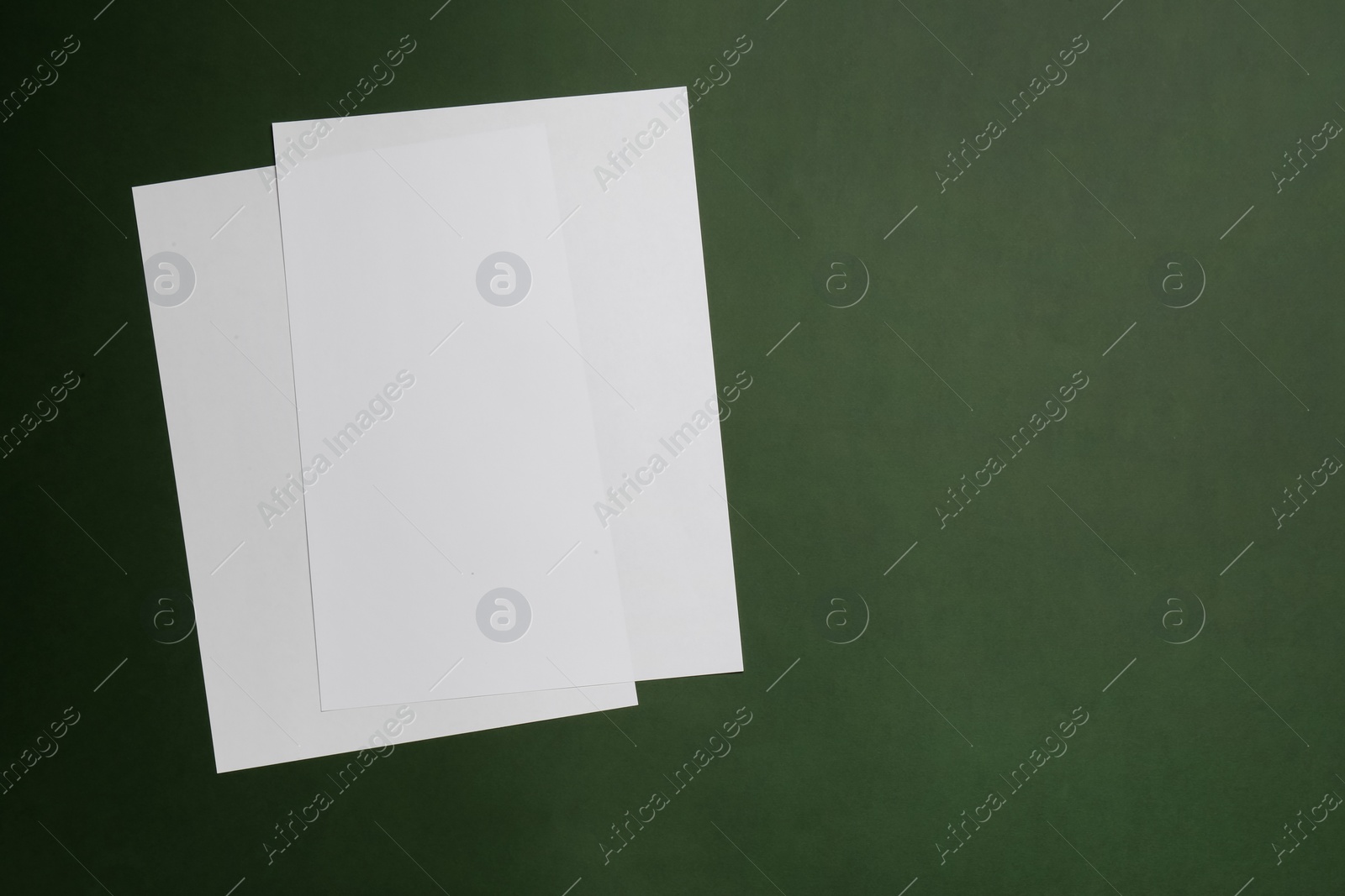 Photo of White paper sheets on dark green background, top view. Space for text