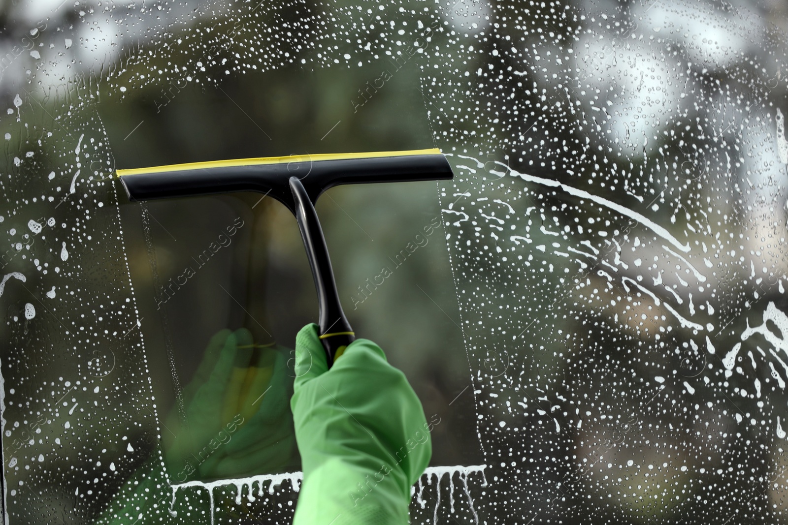 Photo of Woman cleaning glass with squeegee indoors, closeup