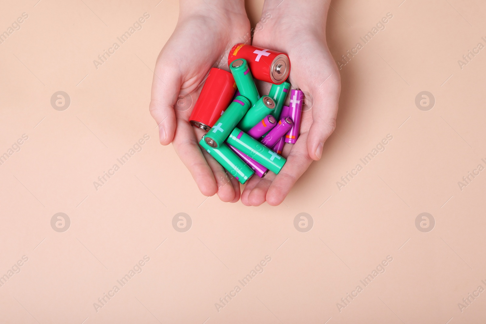 Photo of Woman holding many different batteries on beige background, top view