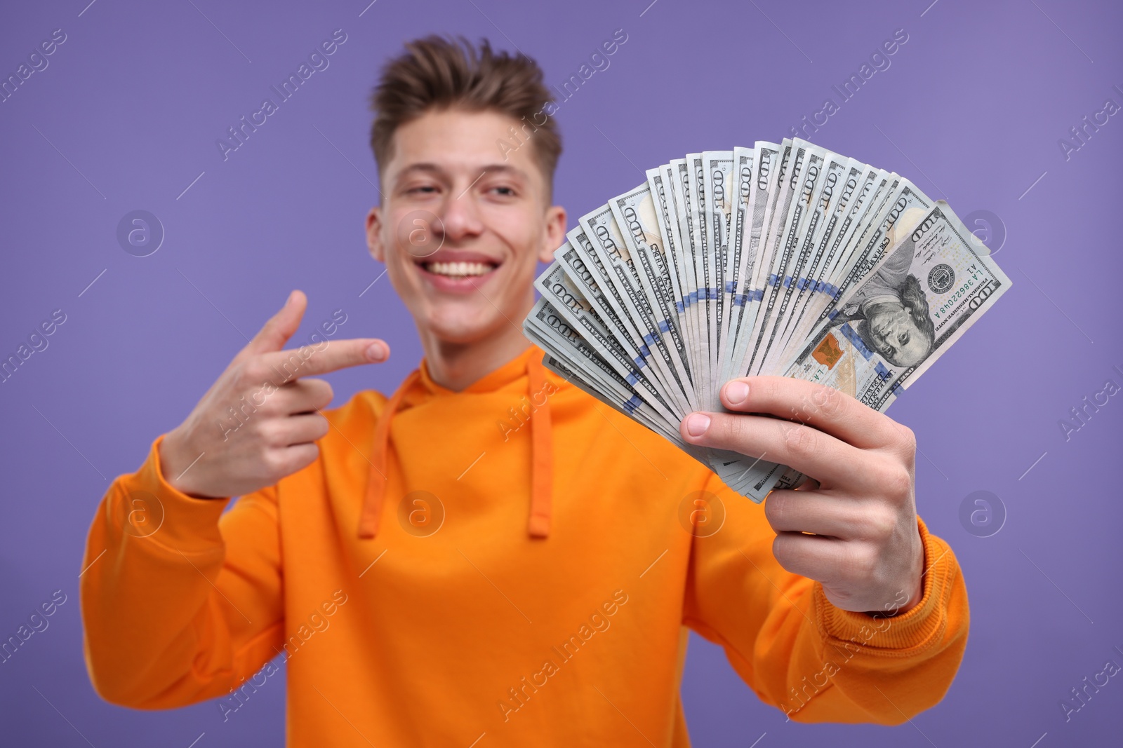 Photo of Happy man pointing at money on purple background, selective focus