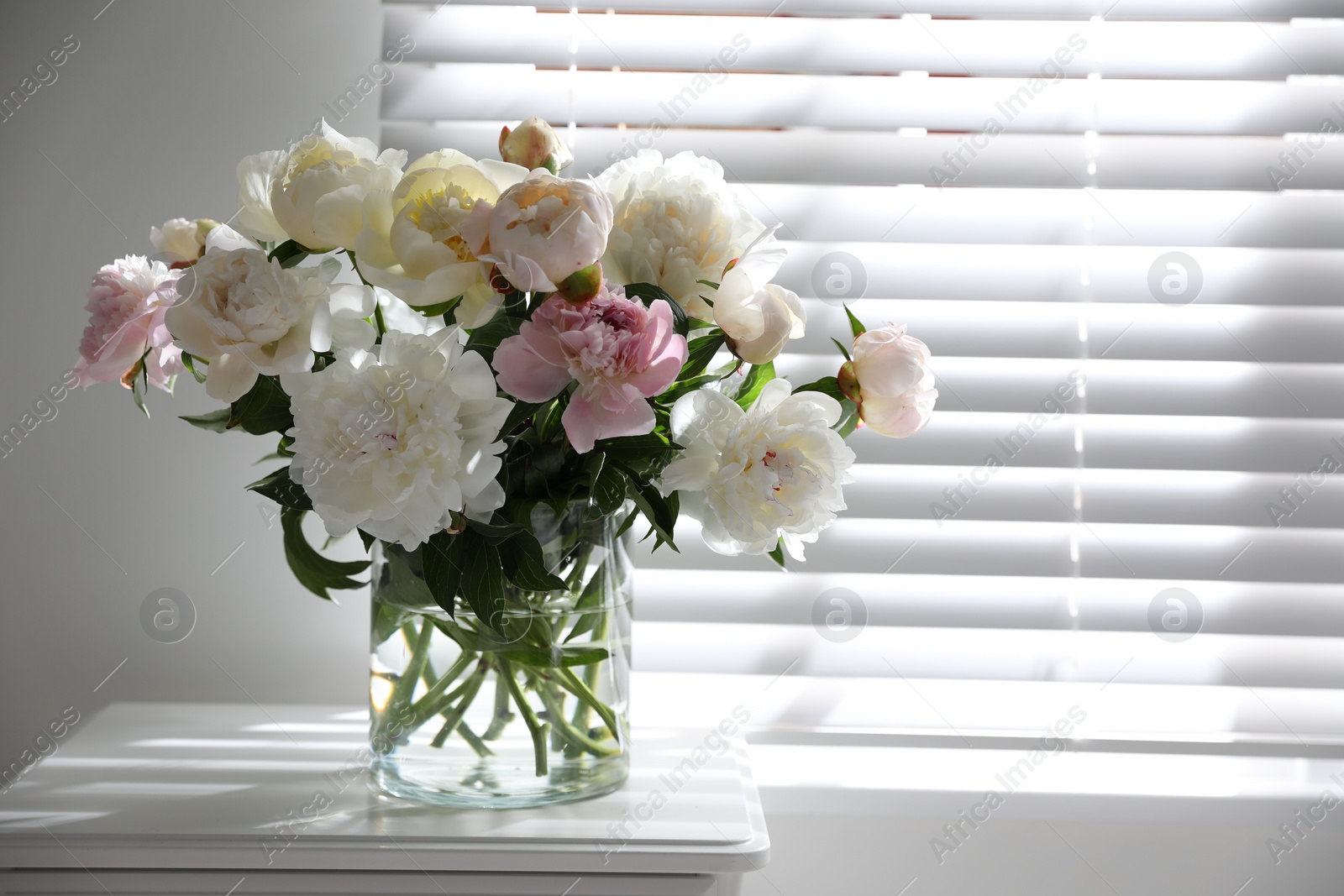 Photo of Beautiful peonies in vase on table near window indoors