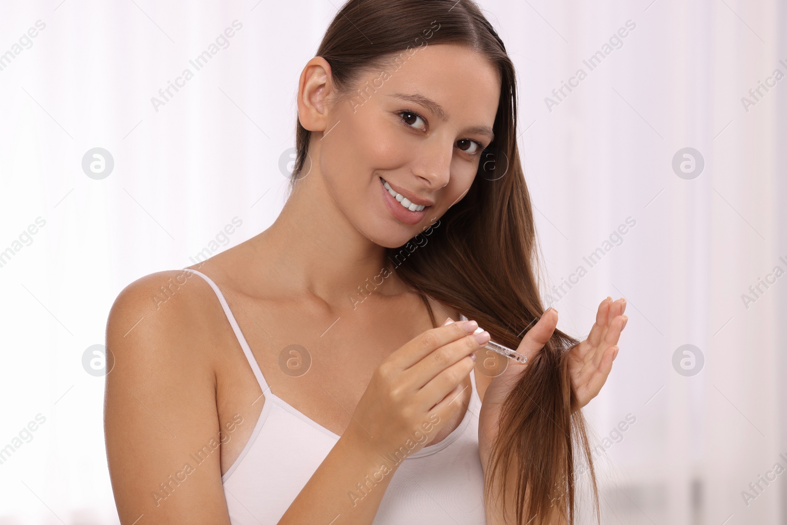 Photo of Beautiful woman applying serum onto hair indoors