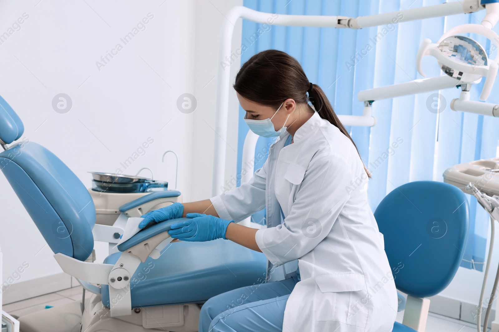 Photo of Professional dentist in white coat and medical mask cleaning workplace indoors