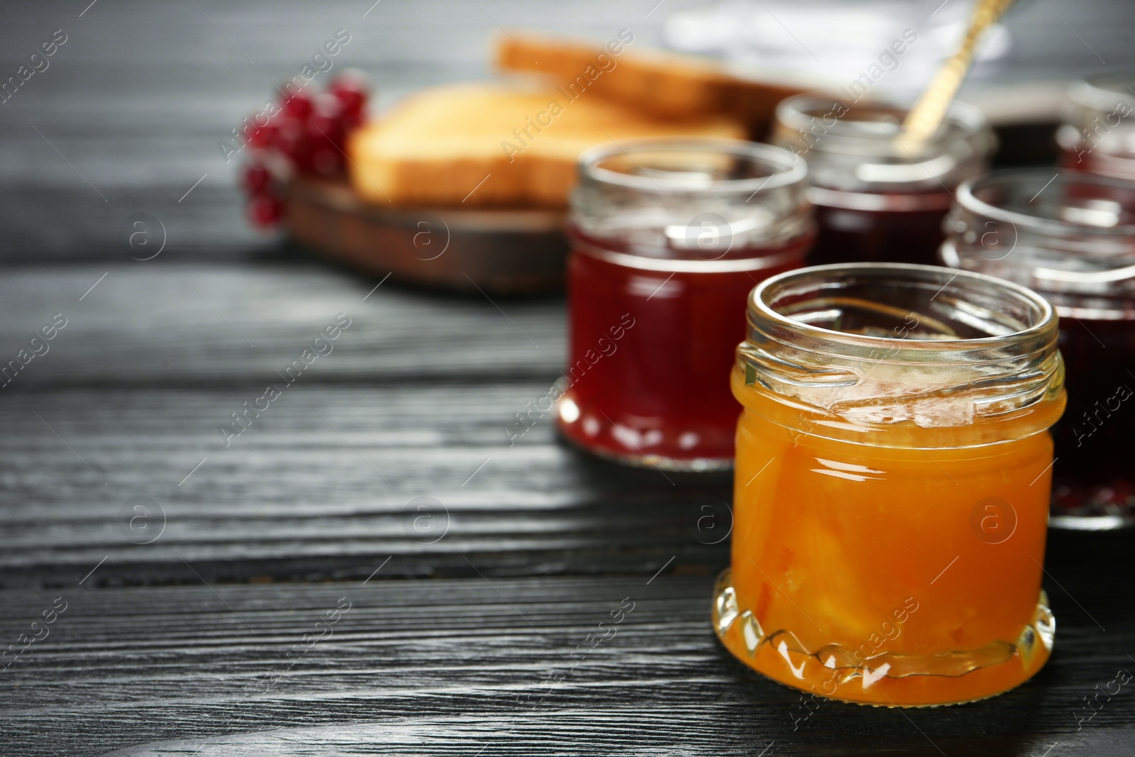 Photo of Jars of different jams on black wooden table, space for text