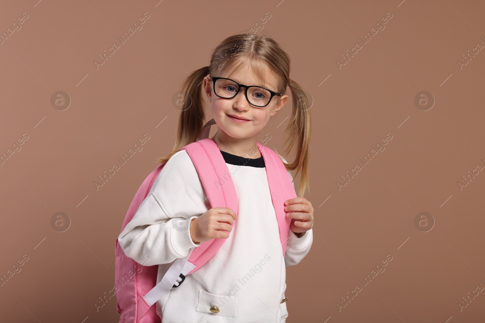 Photo of Happy schoolgirl in glasses with backpack on brown background