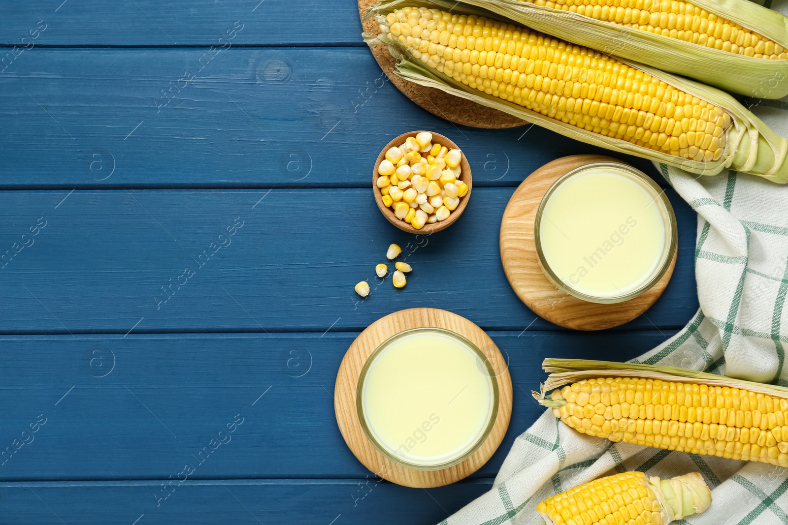 Photo of Tasty fresh corn milk in glasses and cobs on blue wooden table, flat lay. Space for text