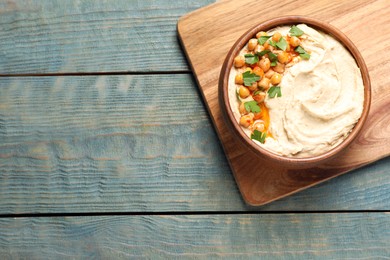 Photo of Bowl of tasty hummus with chickpeas and parsley on wooden table, top view. Space for text