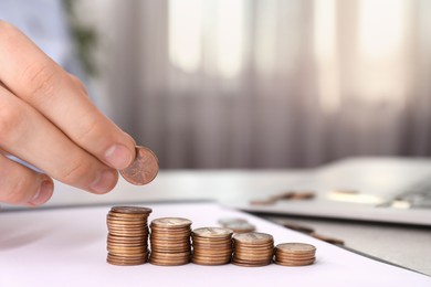 Man stacking coins at table indoors, closeup