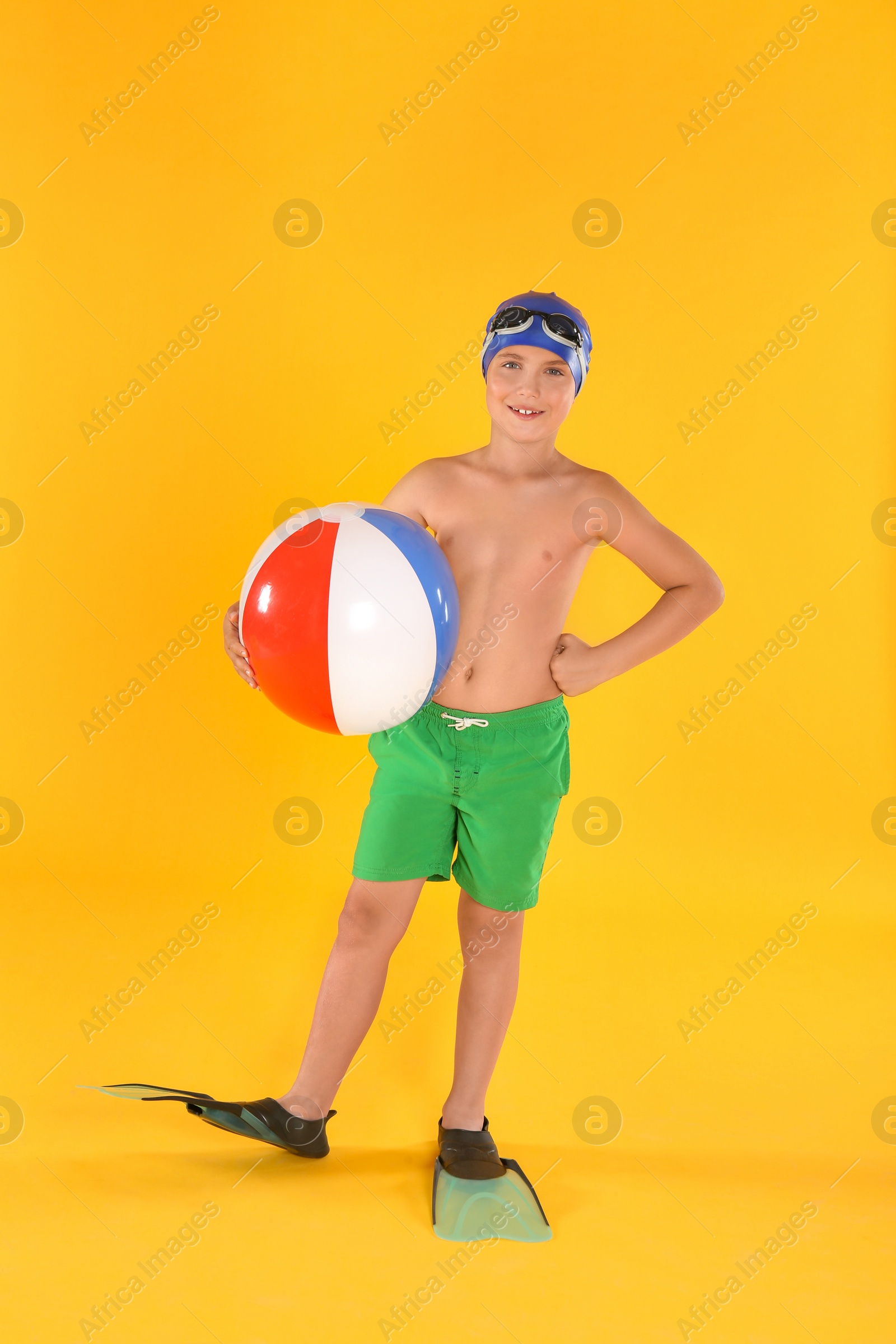 Photo of Cute little child in beachwear with bright inflatable ball on yellow background